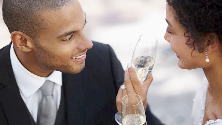 A couple is dressed formally, smiling, and toasting with glasses of champagne. They seem to be at a celebratory event, perhaps a wedding.