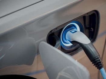 An electric vehicle is being charged, with a blue and black charging cable connected to the car's charging port, seen in close-up.