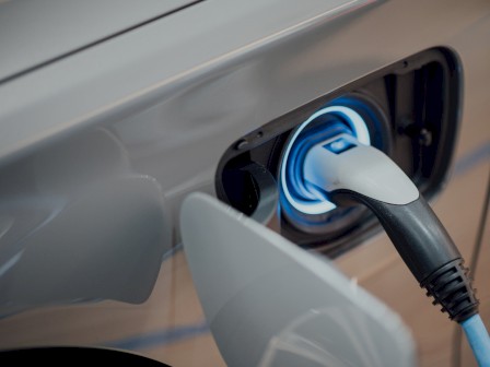 An electric vehicle is being charged, with a blue and black charging cable connected to the car's charging port, seen in close-up.