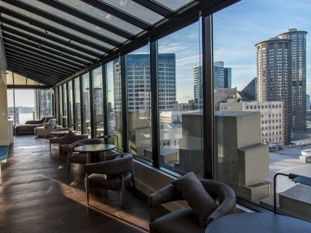 This image shows a modern indoor lounge area with large glass windows providing a panoramic view of a city skyline with tall buildings.