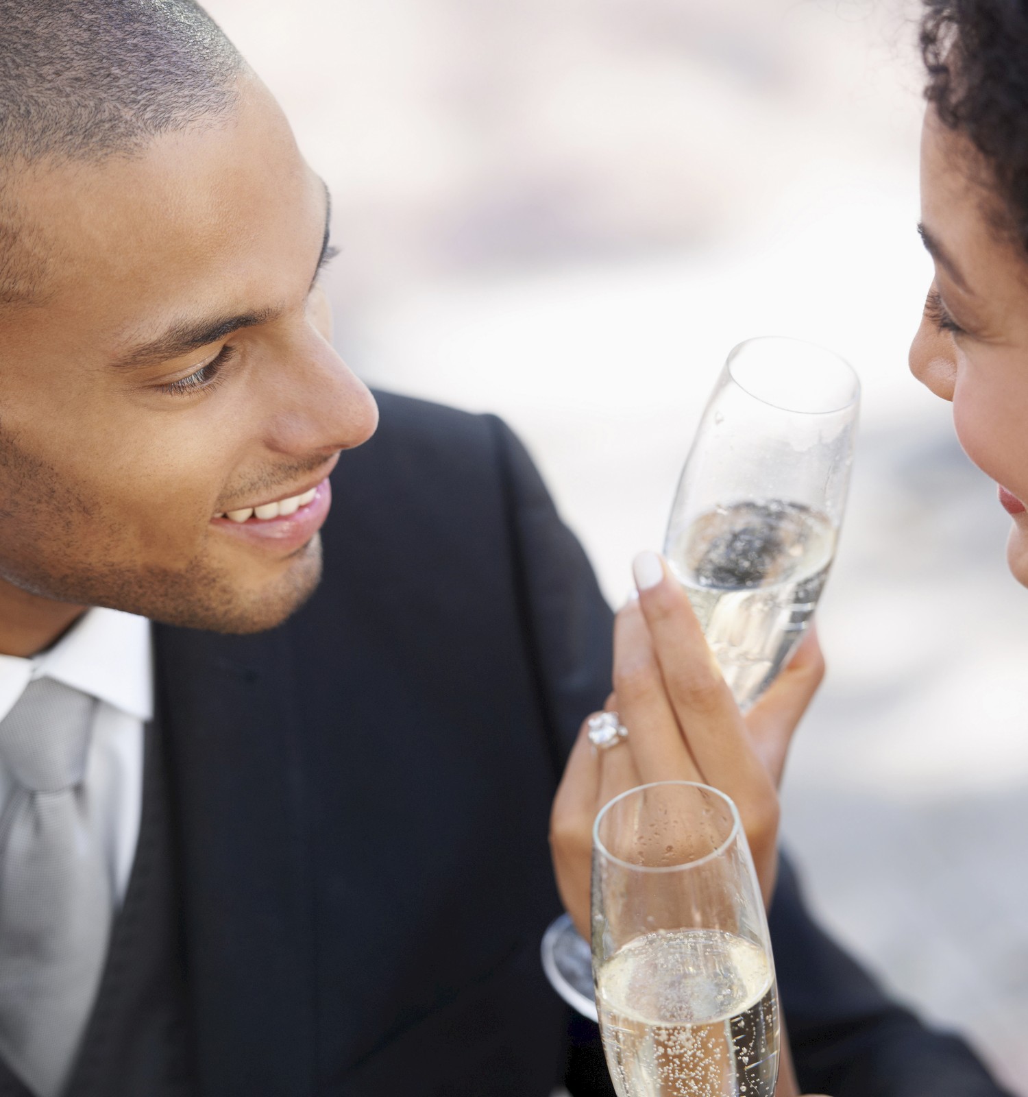 A couple dressed in formal attire smiles at each other while holding glasses of champagne, suggesting a celebratory occasion, possibly a wedding, ending the sentence.