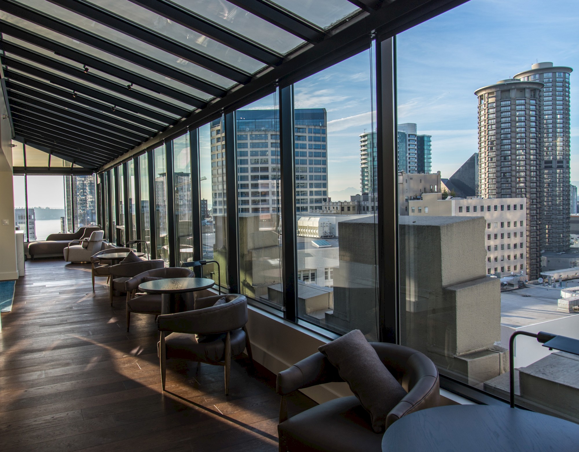 A modern lounge area with floor-to-ceiling windows offering a view of a cityscape with tall buildings and a clear blue sky ending the sentence.