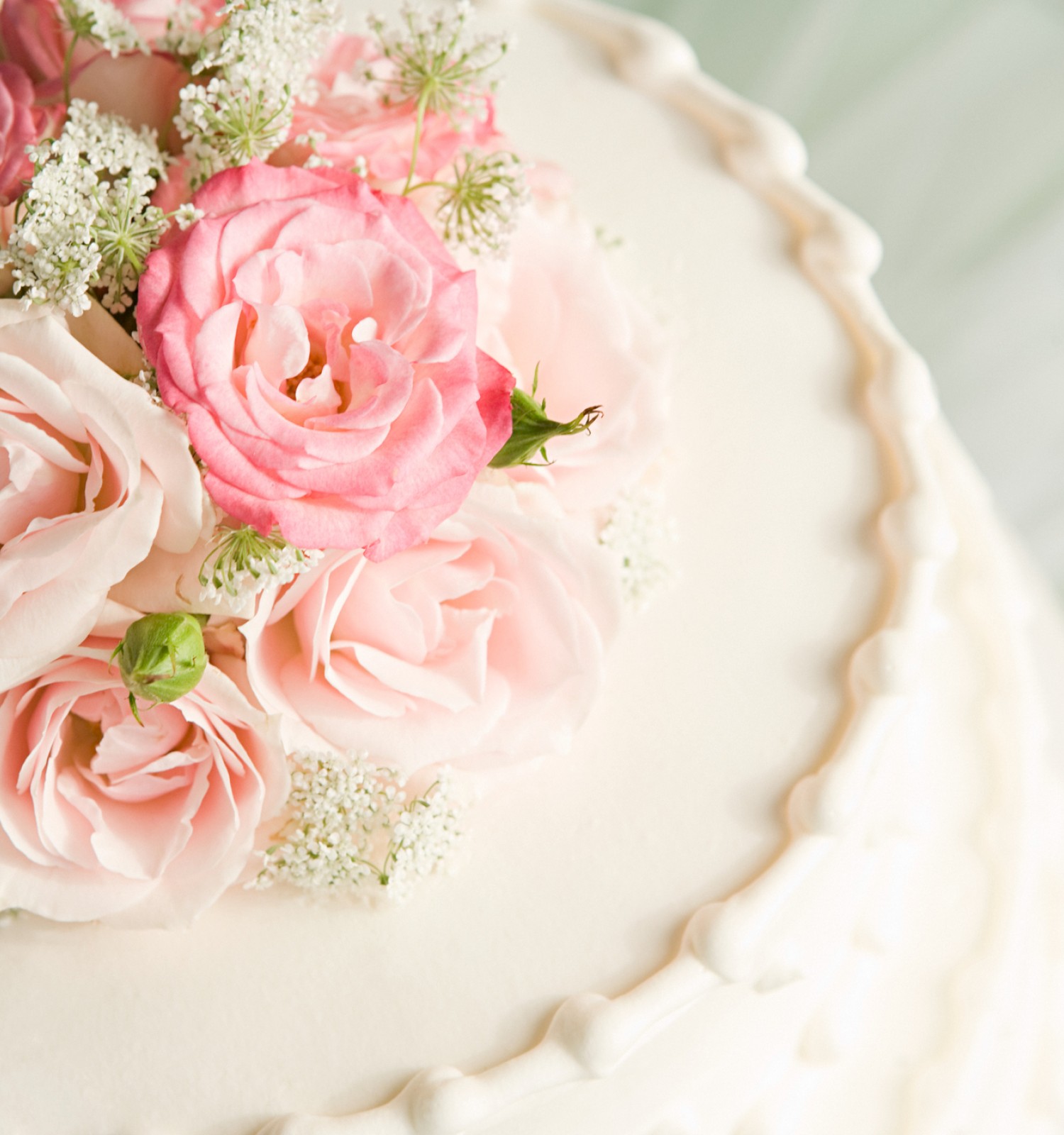 The image shows a close-up of a white cake decorated with pink and white flowers on top, likely for a wedding or special occasion.