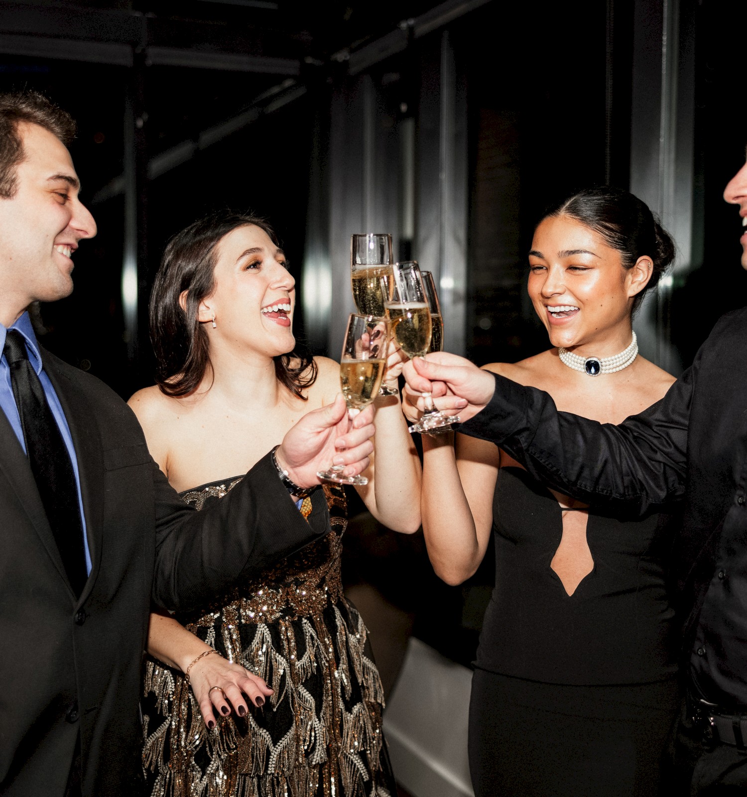 Four people dressed formally are smiling while toasting with champagne glasses at a celebration or party.