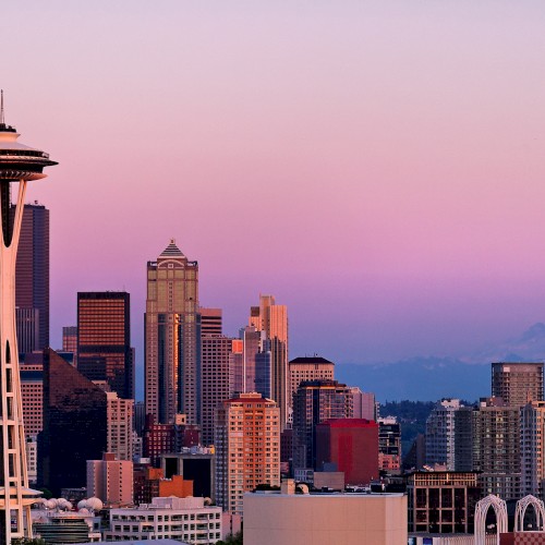 The image shows the Seattle skyline with the Space Needle in the foreground and Mount Rainier in the background during a colorful sunset.