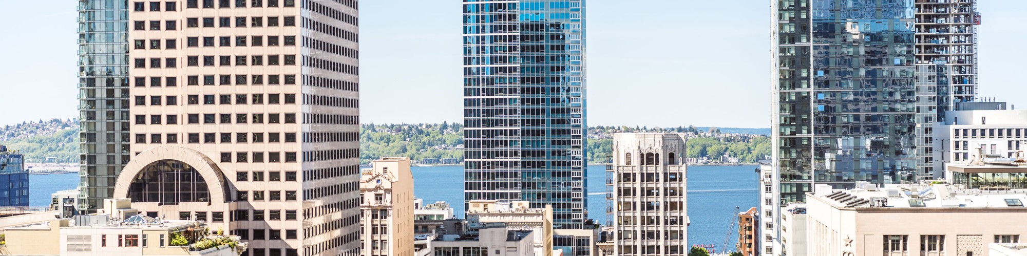 A cityscape view featuring modern skyscrapers with glass facades and a body of water in the background, seen from a balcony.